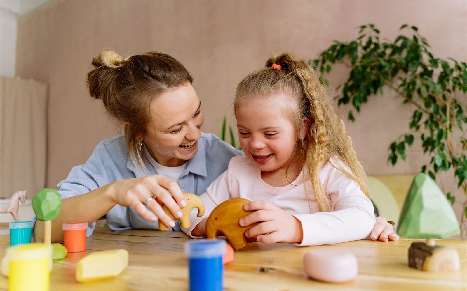 A support worker and a smiling child playing together with wooden animal toys